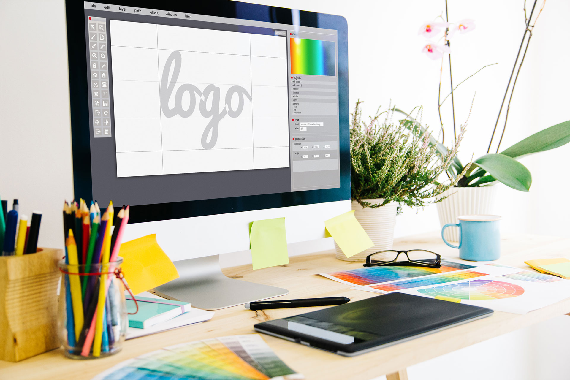 Mesa de um designer gráfico com paletas de cor, caderno, lápis e desenho de logotipo no ecrã